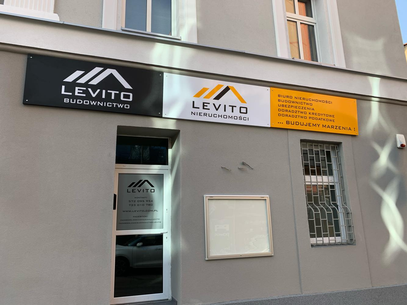 Elewacja budynku z trzema szyldami firmy Levito: Budownictwo, Nieruchomości, oraz Biuro Nieruchomości z dodatkowymi usługami doradczymi i budowlanymi. Na szyldach logo firmy z nazwą Levito.