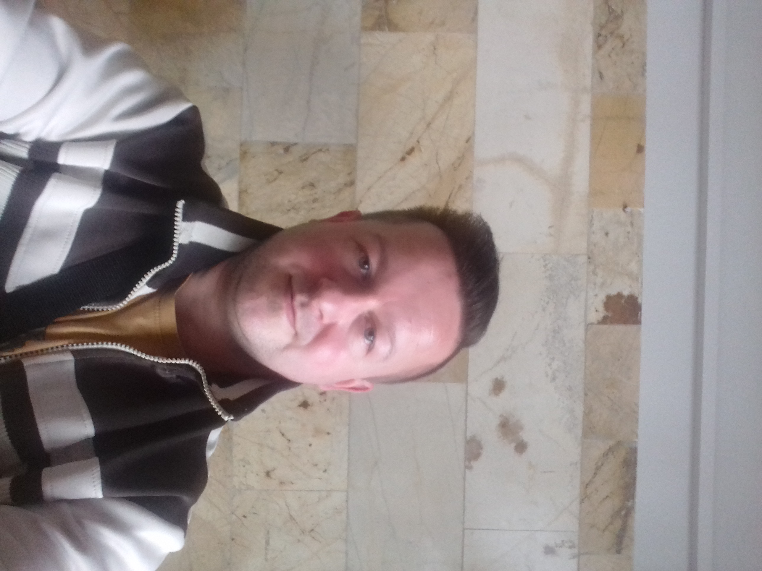 Mężczyzna w bluzie z białymi paskami, widok z góry na marmurowej podłodze.