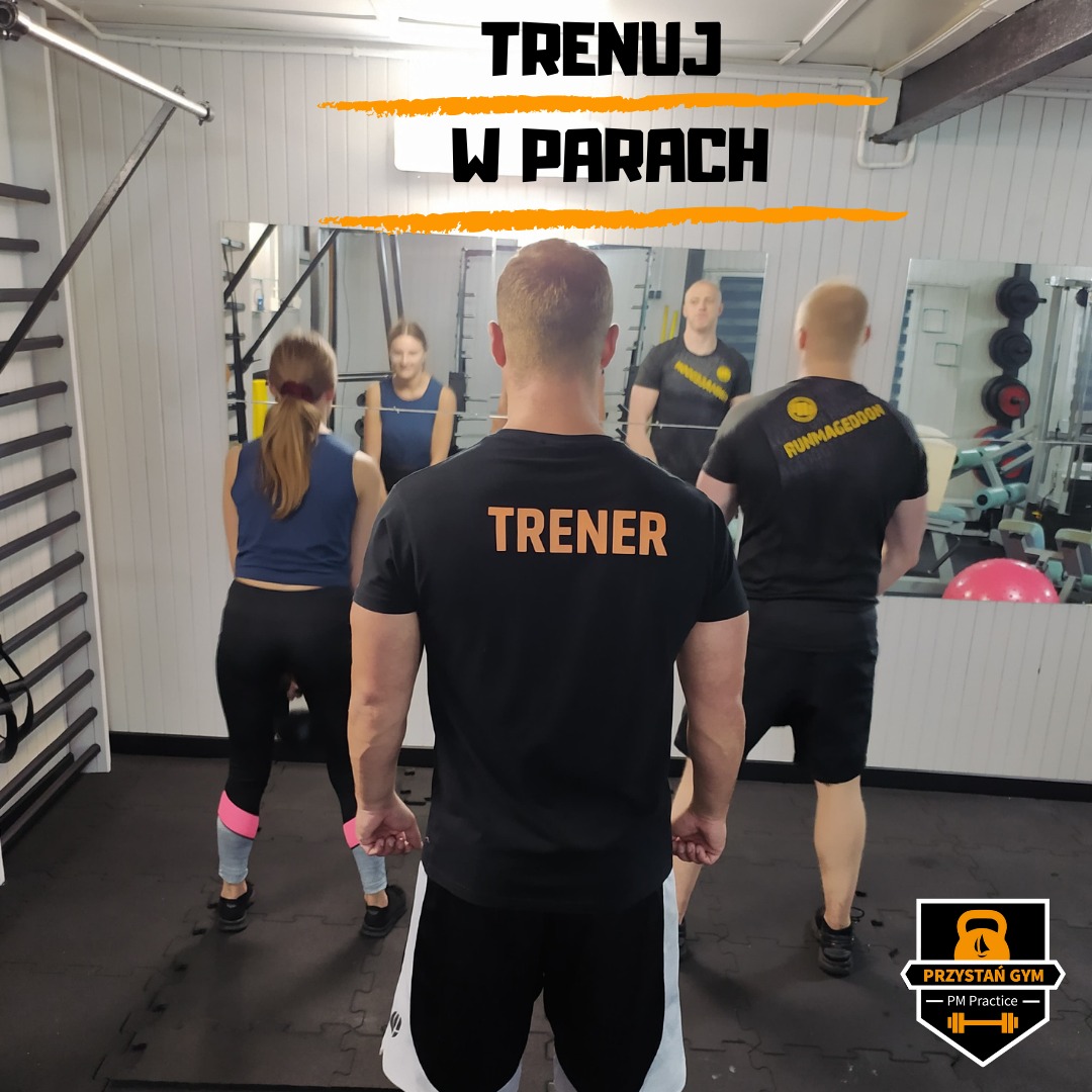 Trener z napisem 'TRENER' na plecach obserwuje ćwiczących w parach w sali gimnastycznej z lustrami.