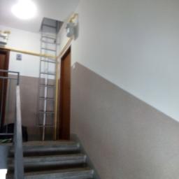 Remontowa Budowlana Igła Stan - Klatka schodowa w bloku z drabina oparta o ścianę, widoczne świeżo pomalowane ściany w dwóch odcieniach szarości.
