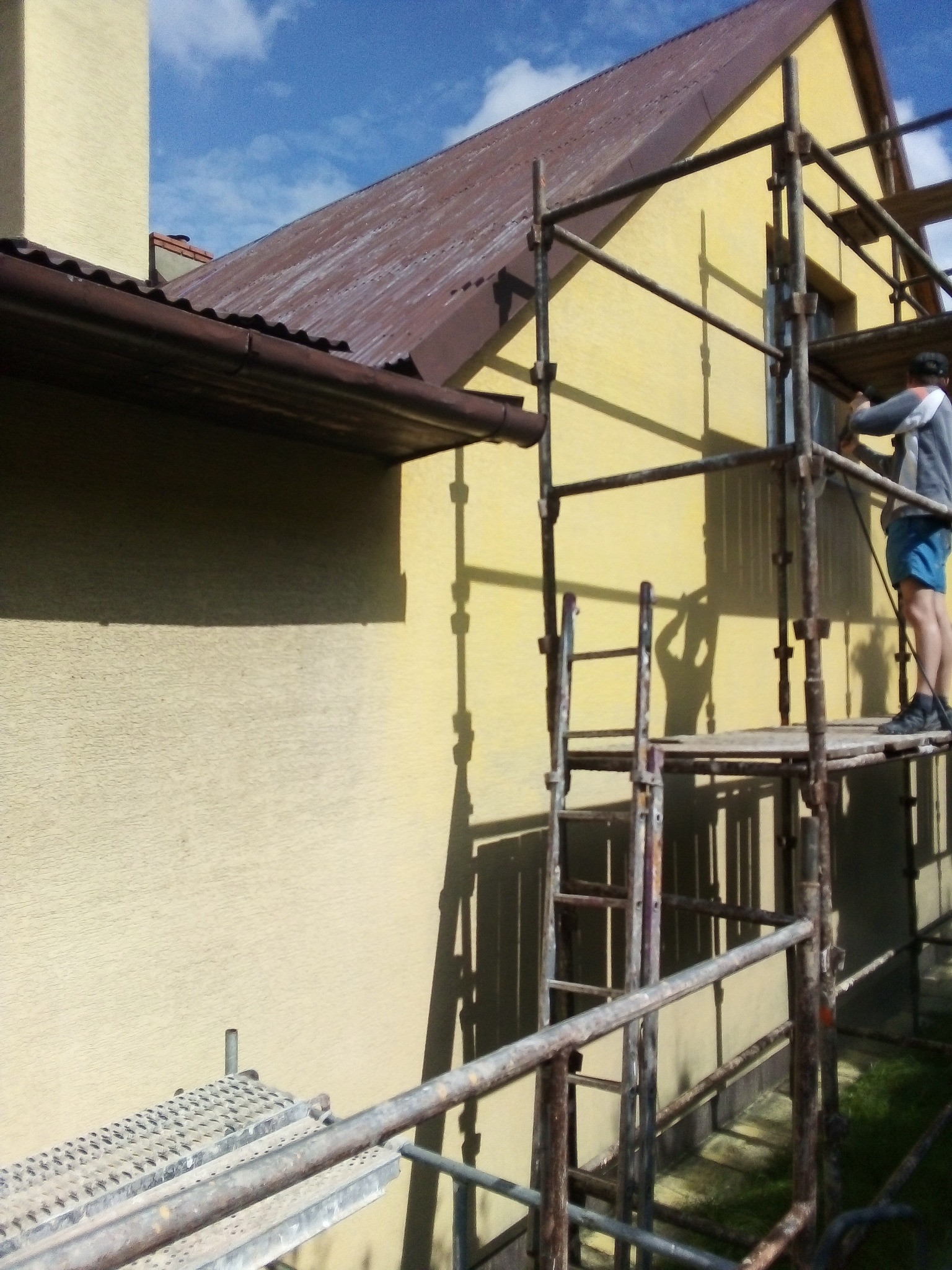 Pracownik na rusztowaniu w Andrychowie przygotowuje elewację budynku do prac wykończeniowych, widoczny cień pracownika na ścianie.