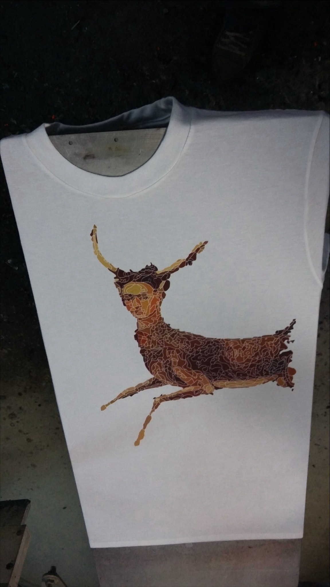 Biała koszulka z graficznym nadrukiem przedstawiającym hybrydę kobiety i jelenia w odcieniach brązu, leżąca płasko na powierzchni.