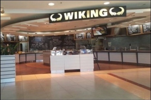 Wnętrze lokalu gastronomicznego 'Wiking' z menu wypisanym na tablicy kredowej, widoczne blaty i ekspozycja potraw, oświetlenie sufitowe.