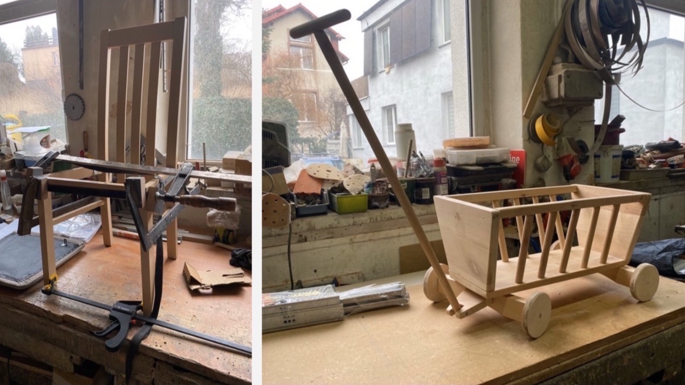 Warsztatowy widok: krzesło w trakcie naprawy z użyciem ścisków stolarskich obok okna oraz ręcznie wykonana drewniana zabawka - wózek z dyszlem na stole, w tle okno.