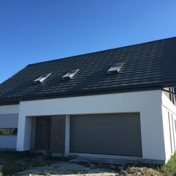 COMFY Piotr Puszkarski - Nowoczesny dom jednorodzinny z grafitową bramą garażową i trzema oknami dachowymi, na tle błękitnego nieba.