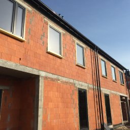 COMFY Piotr Puszkarski - Szeregówka w trakcie budowy, widoczne wstawione okna i drzwi z pianką montażową, ściany z czerwonej cegły.