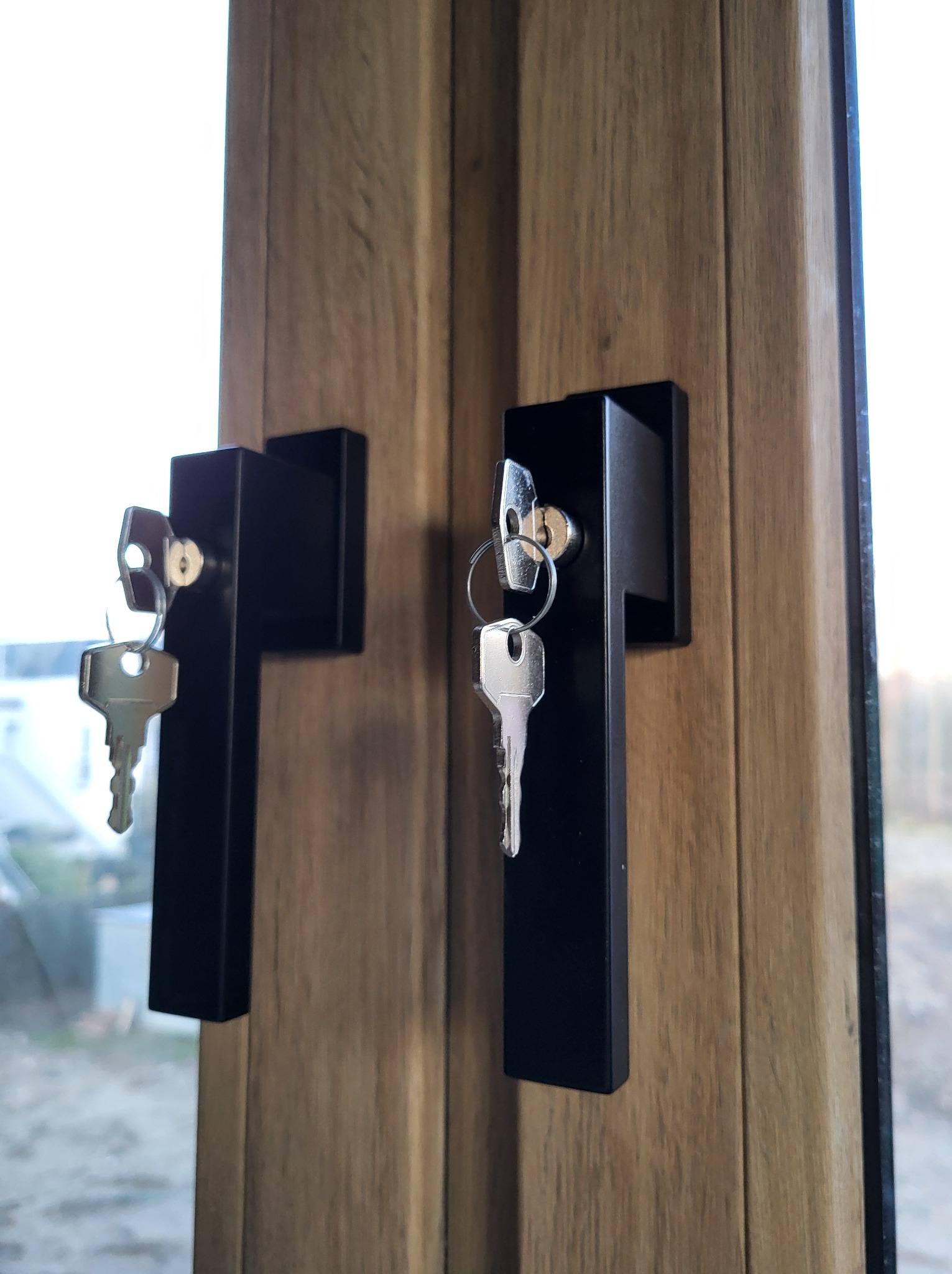 Dwa okna z czarnymi klamkami i kluczami w zamkach, drewnopodobna okleina ramy okiennej.