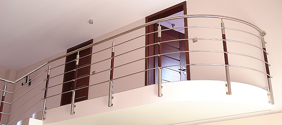 Wewnętrzna balustrada ze stali nierdzewnej z trzema poprzecznymi prętami, zamontowana na antresoli z widokiem na dwoje ciemnych drzwi.