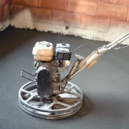 Zacieraczka mechaniczna do betonu na świeżo wylanej posadzce, widoczny fragment ściany z cegły i ślady po szpachlowaniu.