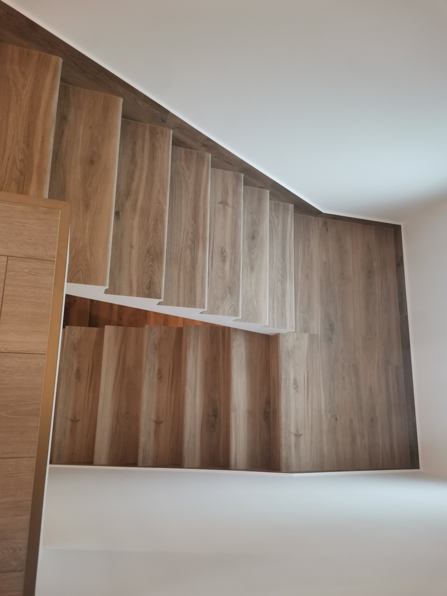 Wykończone schody wewnętrzne z drewnopodobnych paneli, widok z góry, jasne ściany i sufit.