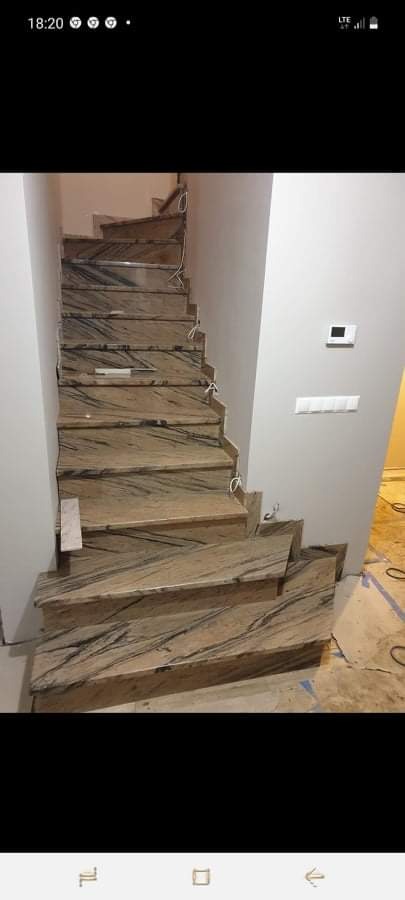 Wykończone schody wewnętrzne z płyt imitujących marmur, z widocznymi przewodami elektrycznymi wystającymi ze ściany i folią zabezpieczającą podłogę.