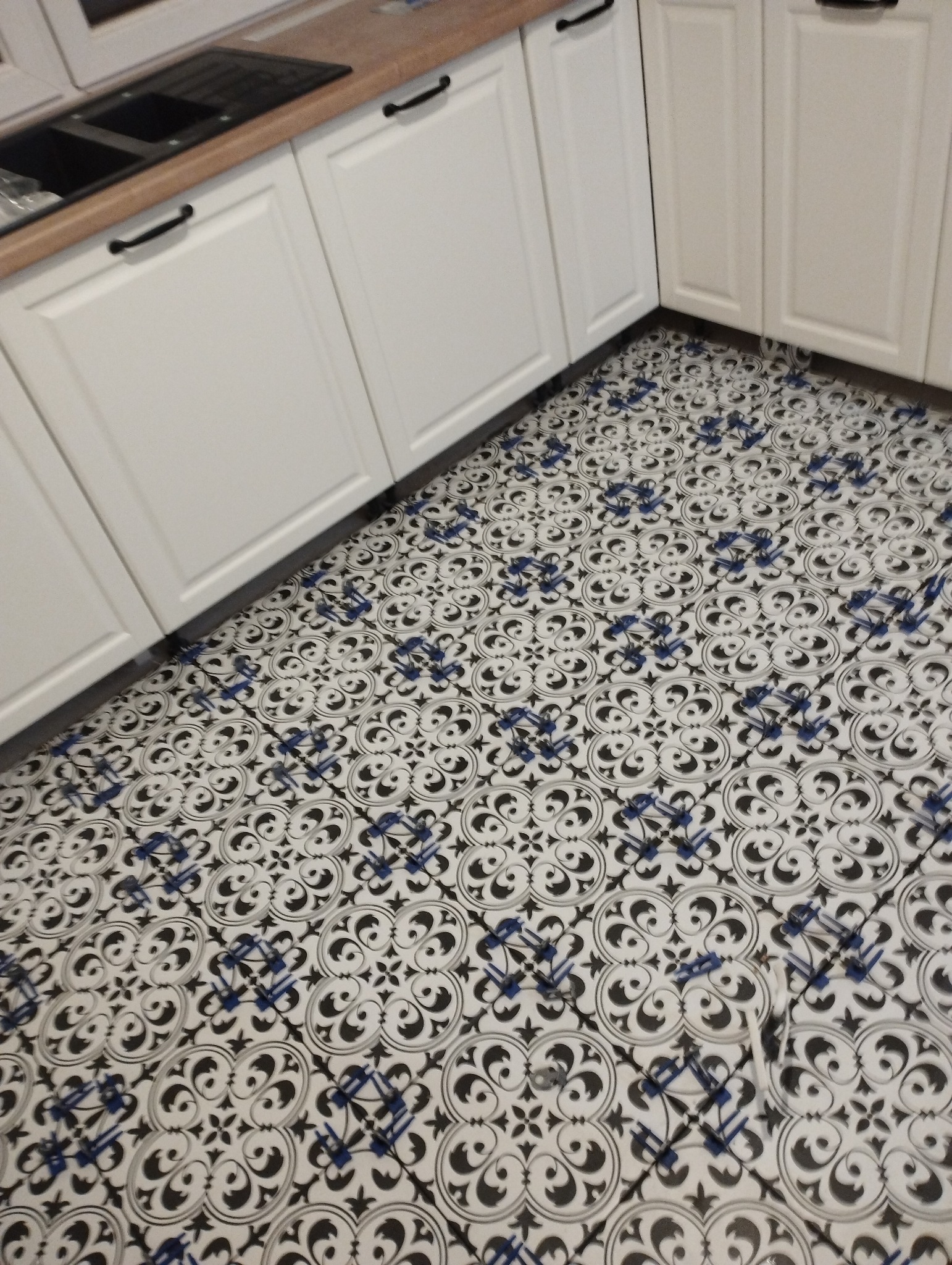 Nowo położona, wzorzysta podłoga w kuchni z białymi szafkami i drewnianym blatem.