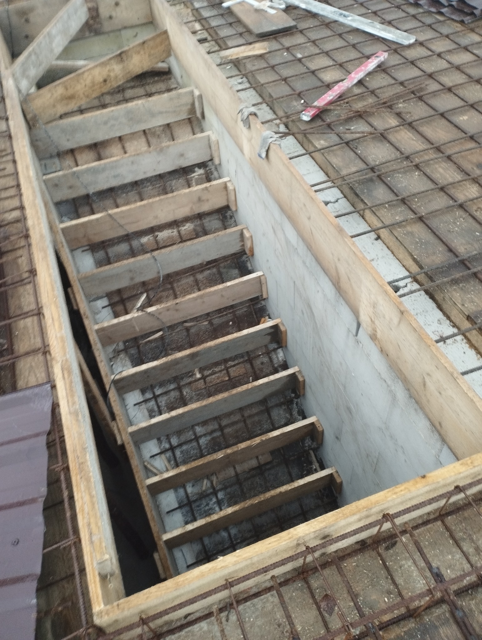 Szare, betonowe schody w trakcie budowy, z widocznym zbrojeniem i drewnianym szalunkiem, oświetlone naturalnym światłem.