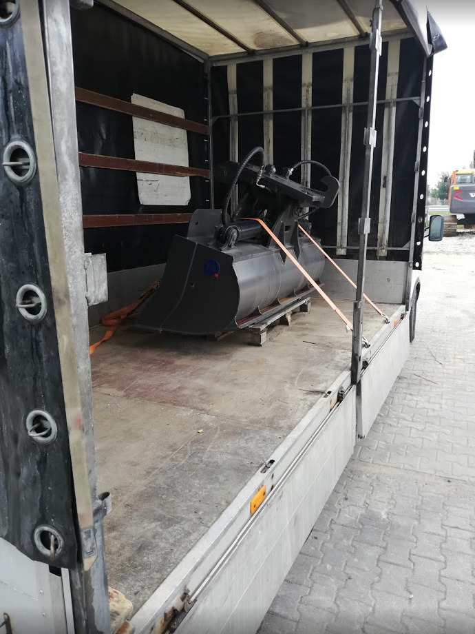 Ciężka łyżka koparki zabezpieczona pasami w przestrzeni ładunkowej pojazdu dostawczego.