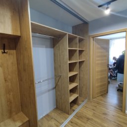 Mebel Pro Dariusz Pieron - Wnętrze szafy wnękowej z półkami i drążkiem na ubrania, widok na otwarte drzwi do pokoju z osobą siedzącą przy biurku