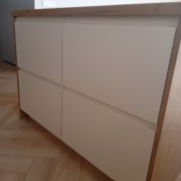 Mebel Pro Dariusz Pieron - Narożna szafka z czterema białymi, gładkimi frontami i drewnianym blatem, dopasowana do parkietu w jodełkę.