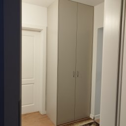 Mebel Pro Dariusz Pieron - Dwudrzwiowa szafa w korytarzu, z widoczną podłogą drewnianą i dywanikiem, obok białe drzwi.