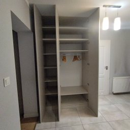 Mebel Pro Dariusz Pieron - Wnętrze szafy z półkami i drążkiem na wieszaki, widoczne wieszaki bez ubrań, oświetlenie sufitowe w tle, jasna kolorystyka wnętrza.