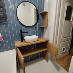 Mebel Pro Dariusz Pieron - Łazienka z umywalką nablatową na drewnianej szafce z otwartymi drzwiczkami, okrągłe lustro i niebieskie płytki na ścianie.