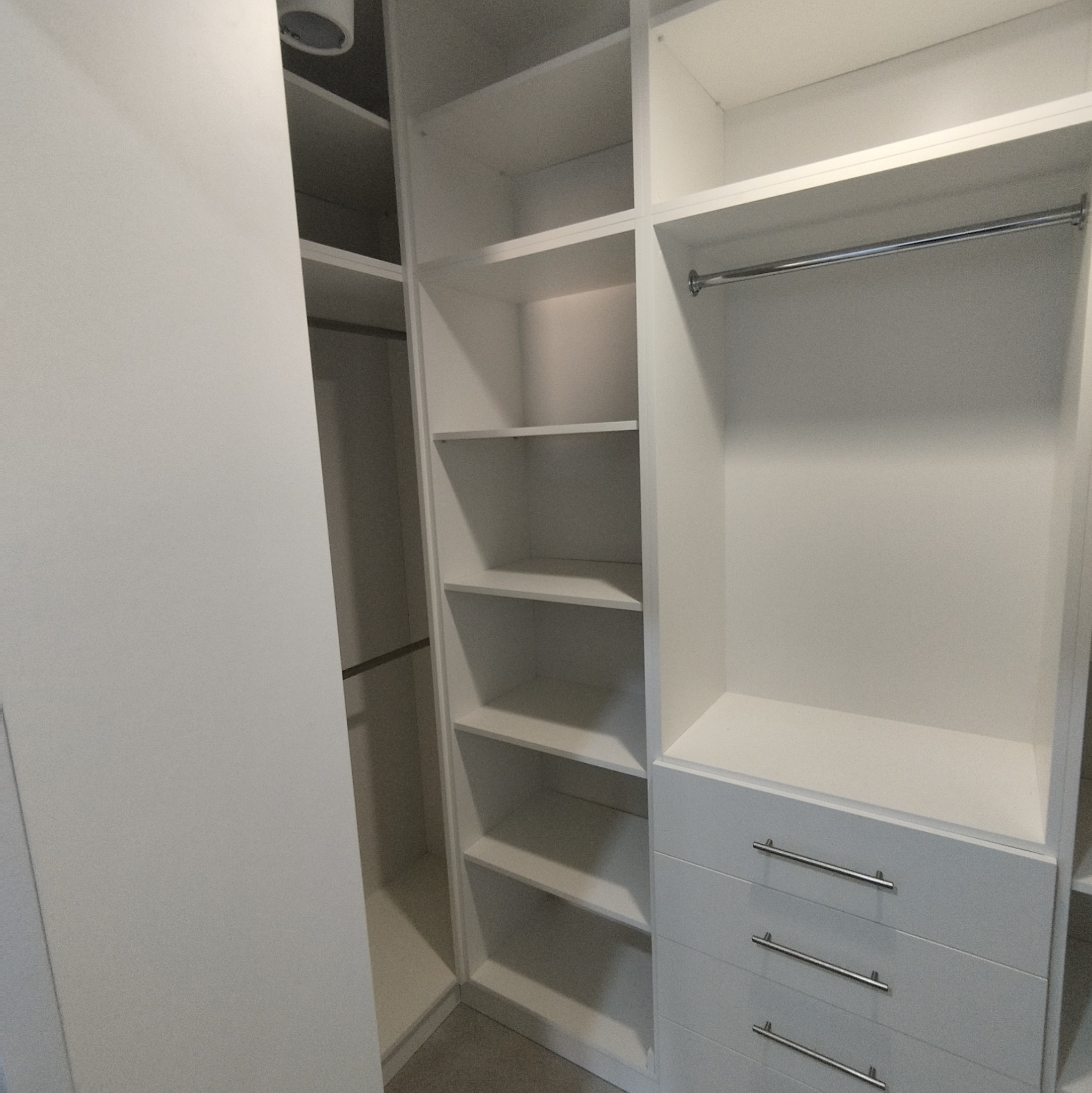 Wnętrze szafy z białymi półkami i szufladami z metalowymi uchwytami, widoczny drążek na ubrania.