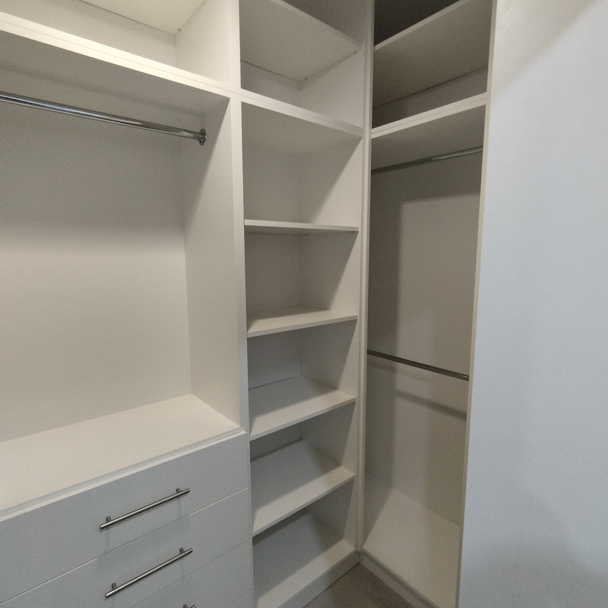 Wnętrze białej szafy wnękowej z szufladami i półkami, widoczny drążek na ubrania.