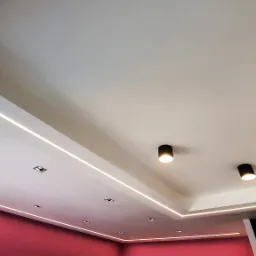 Nowoczesne oświetlenie sufitowe z liniowymi lampami LED i punktowymi reflektorami w kolorze czarnym, ściana pomalowana na różowo.