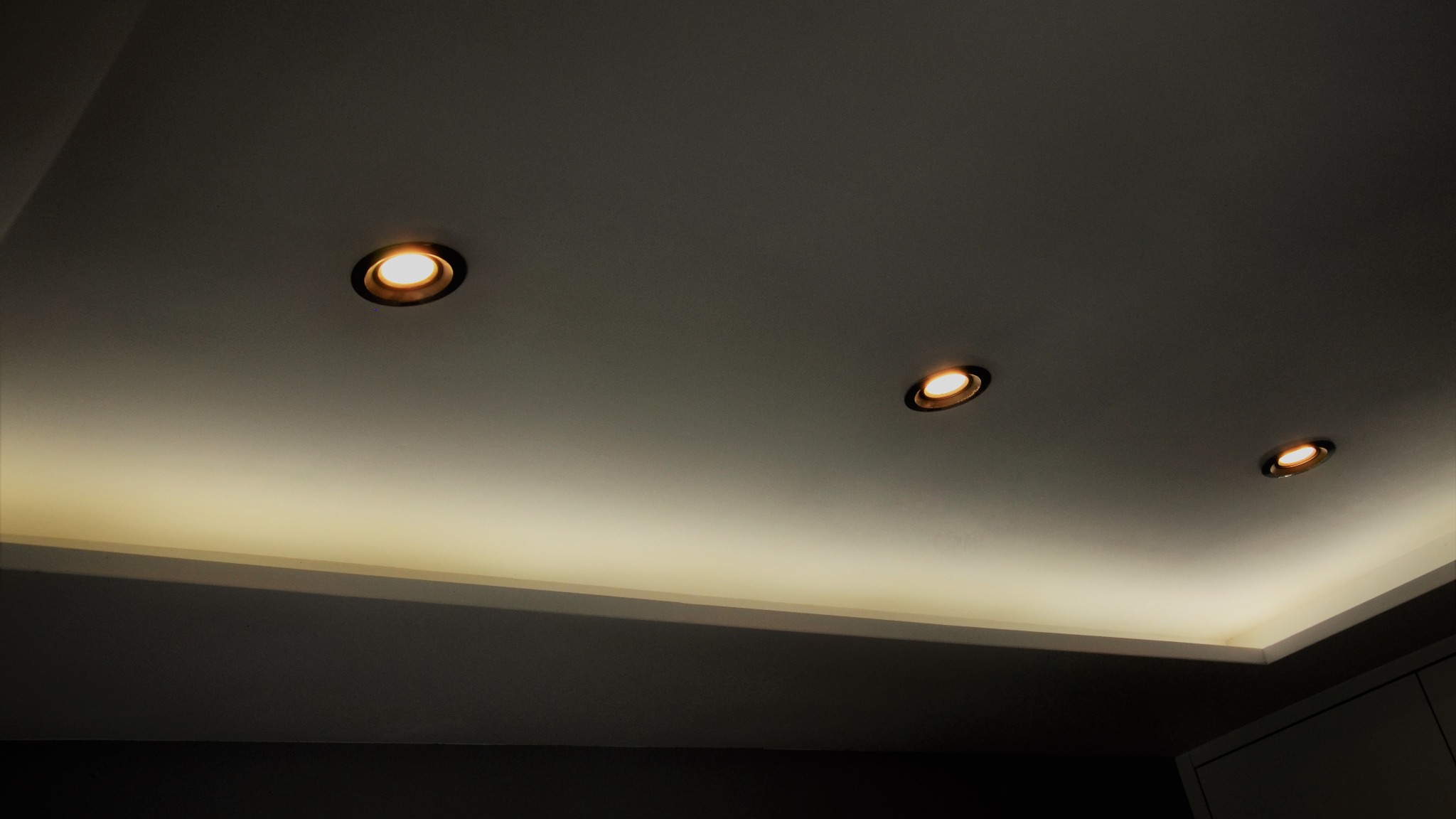 Sufit podwieszany z trzema okrągłymi lampami halogenowymi wpuszczonymi, oświetlenie LED ukryte w szczelinie, ciepłe światło.