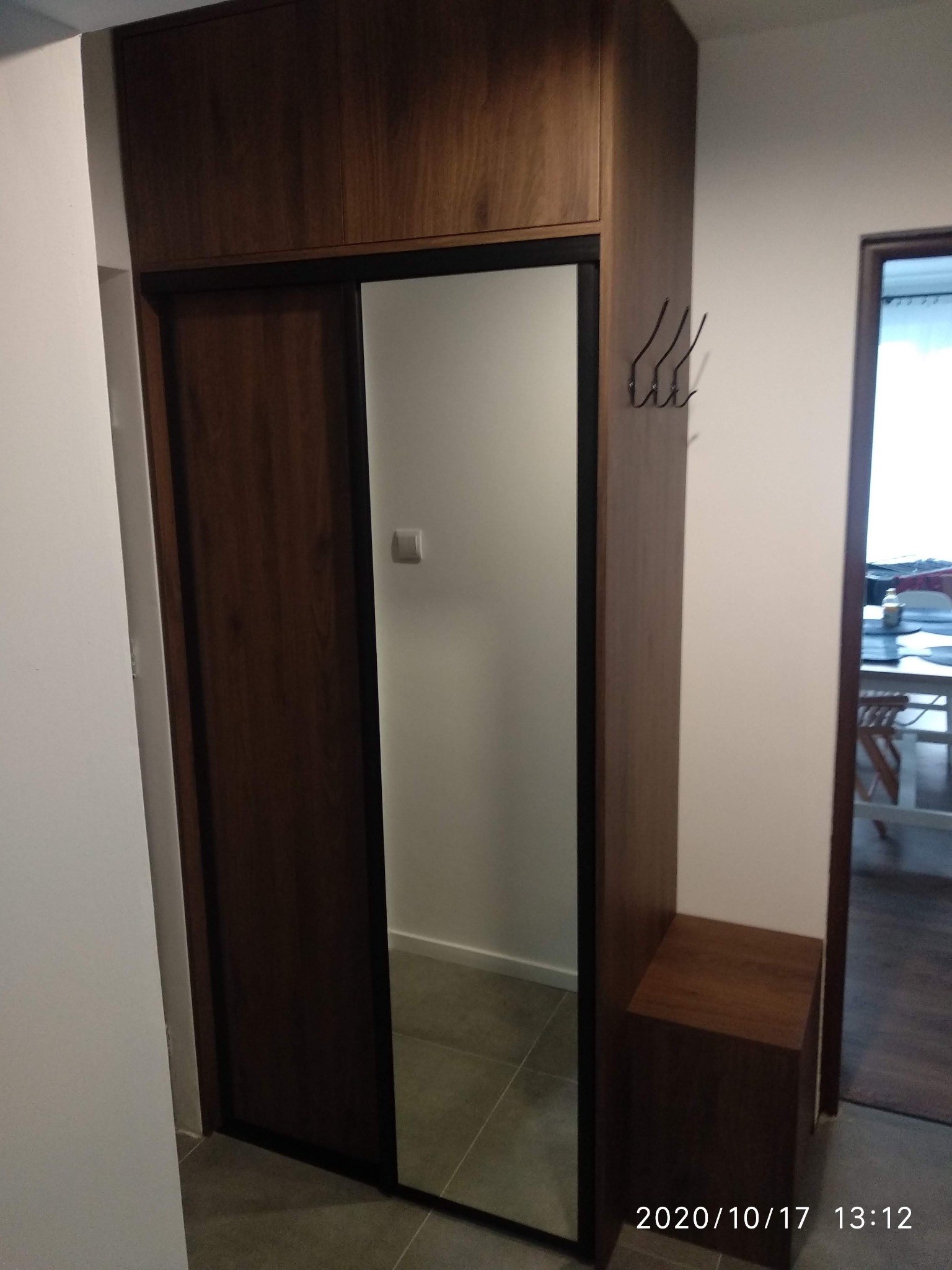 Wysoka szafa z przesuwnymi drzwiami z lustrem w przedpokoju, z wbudowanym siedziskiem i wieszakami na ścianie.