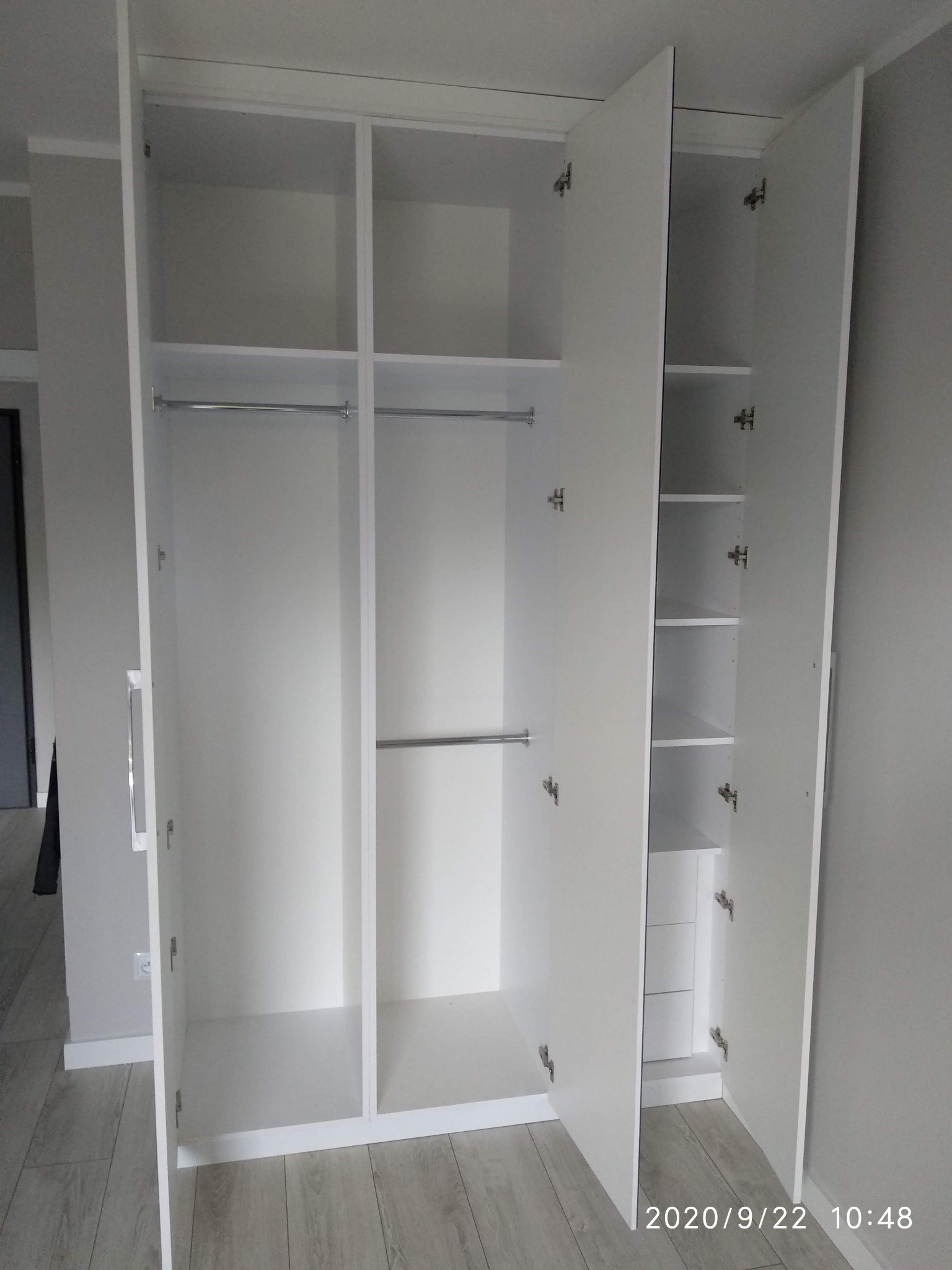 Wnętrze białej, otwartej szafy z drążkami na wieszaki i półkami, widok na zawiasy, proste wykończenie.