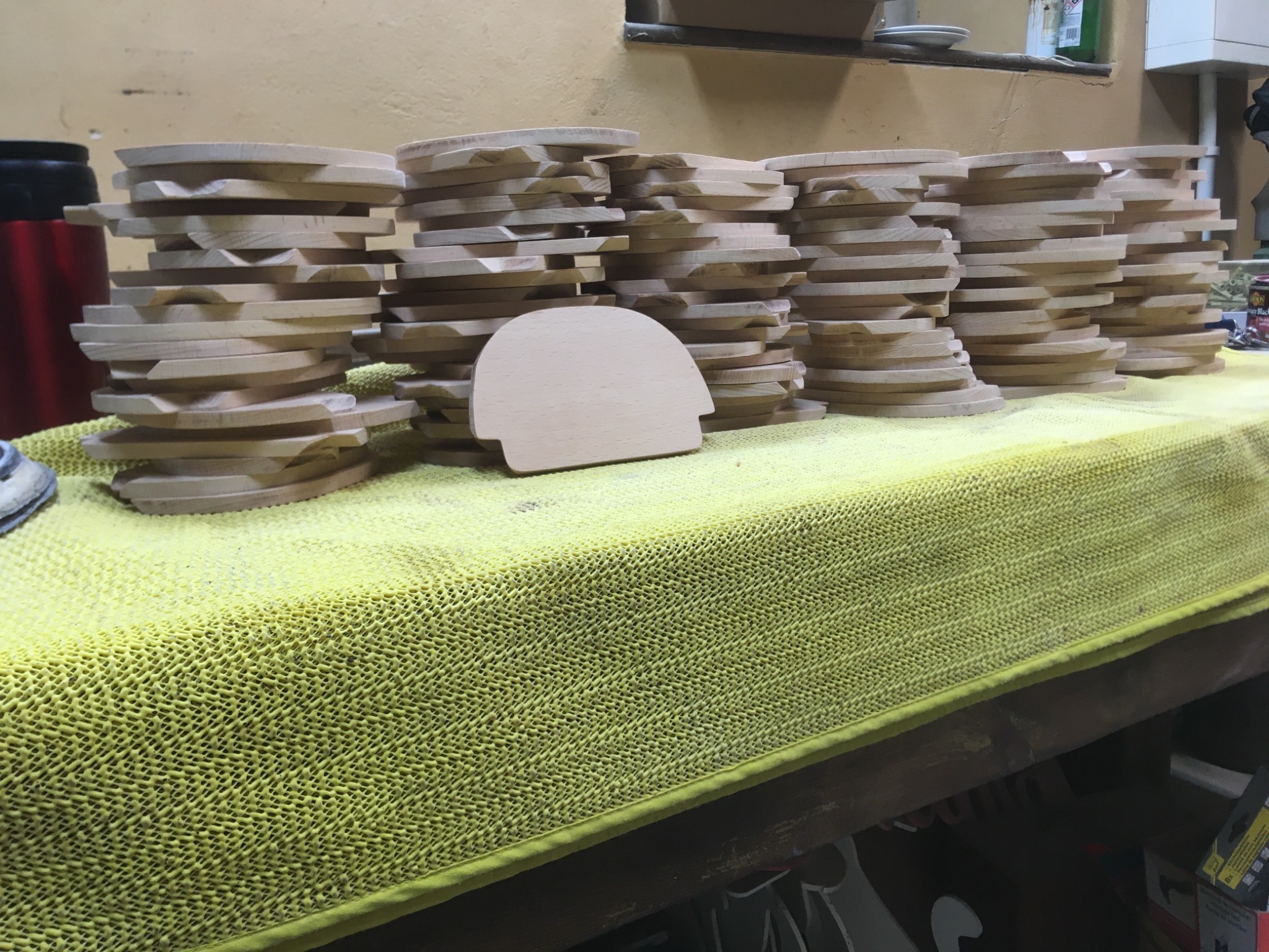 Stosy surowych, drewnianych elementów o zaokrąglonym kształcie na żółtym, teksturowanym blacie roboczym w warsztacie.