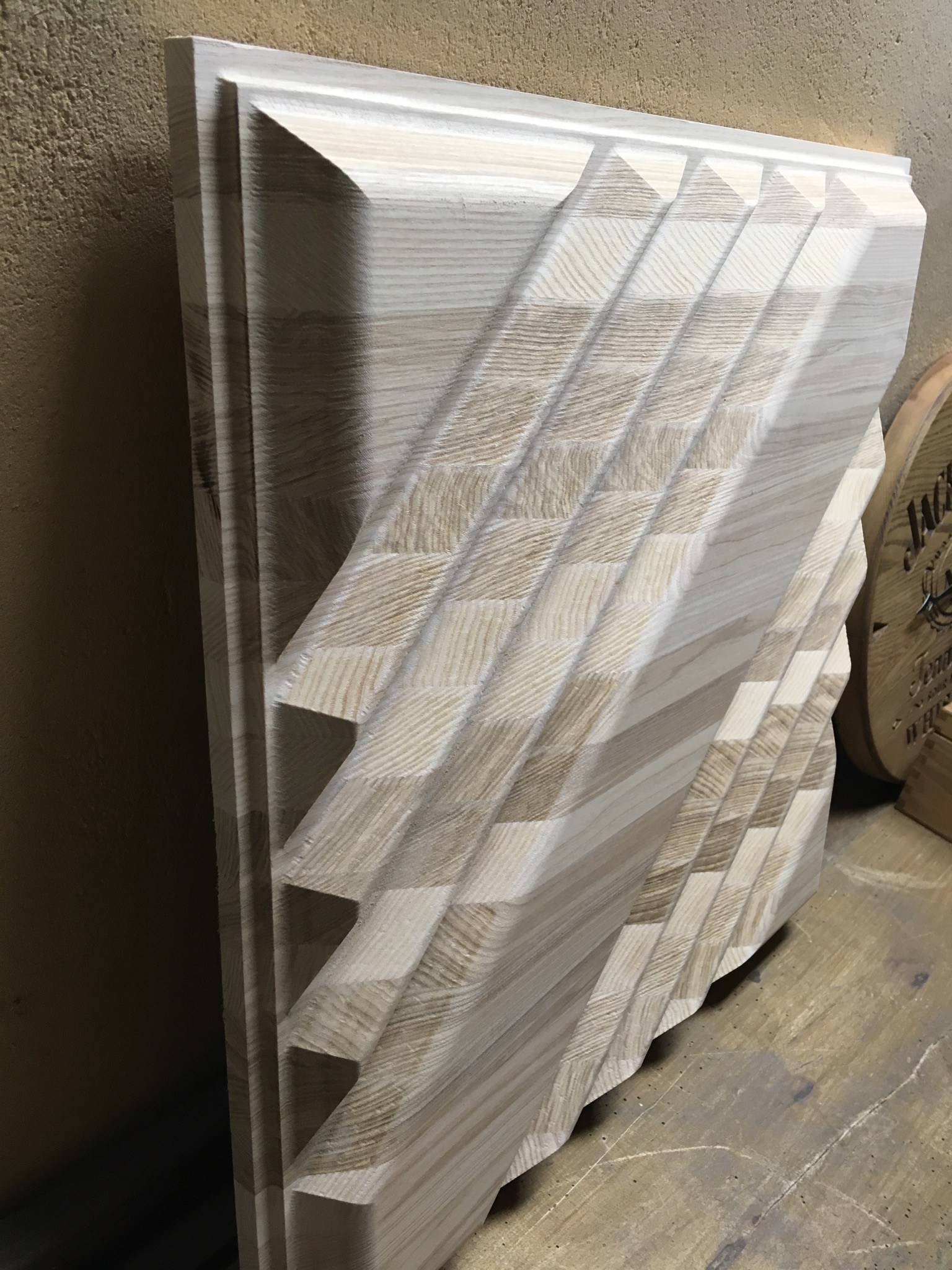 Surowe drewno z rzeźbionym, geometrycznym wzorem w kształcie zygzaka, prawdopodobnie element dekoracyjny lub fragment większej konstrukcji, widoczne słoje drewna.