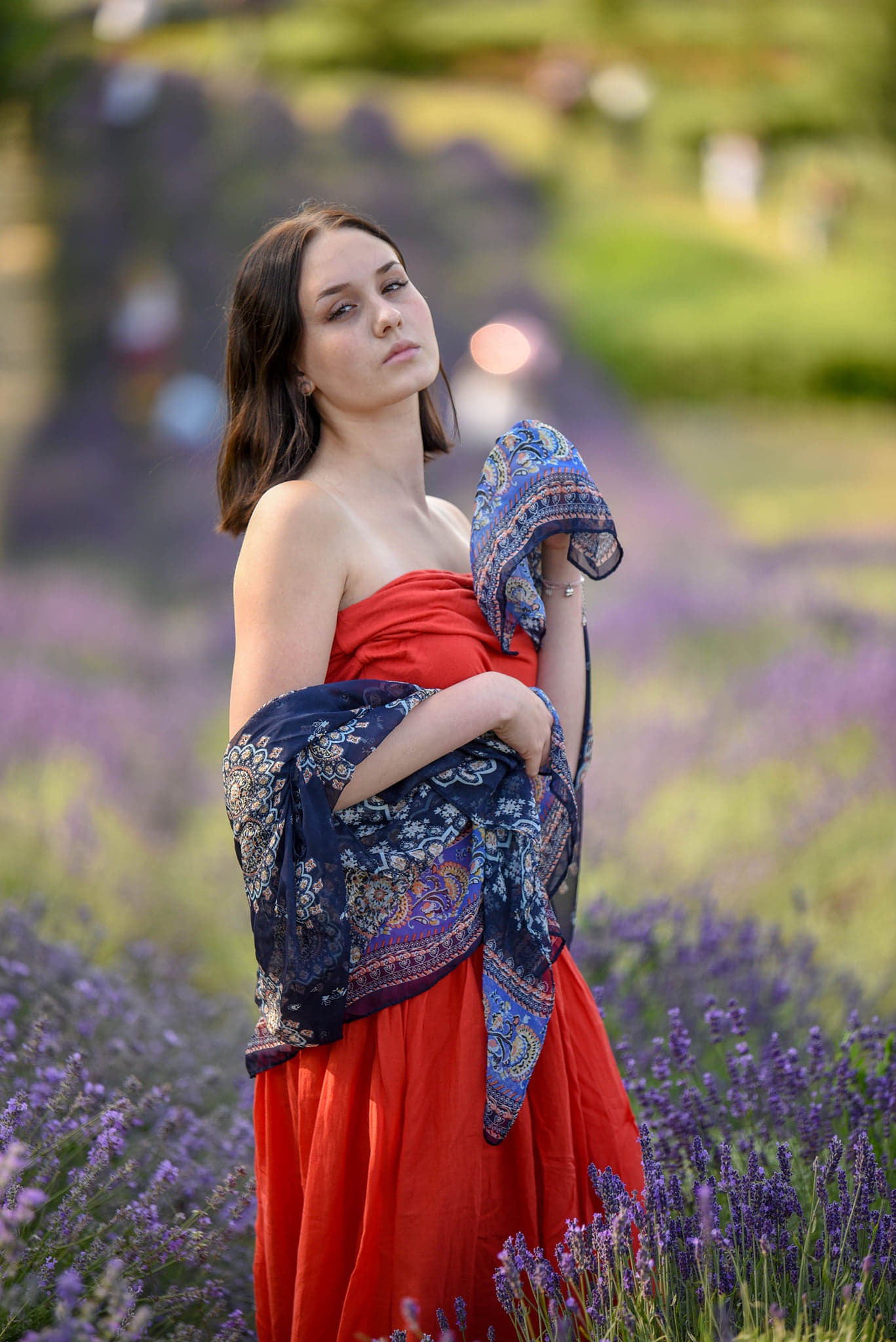 Młoda kobieta w czerwonej sukience i wzorzystej chuście pozuje na tle kwitnącej lawendy.