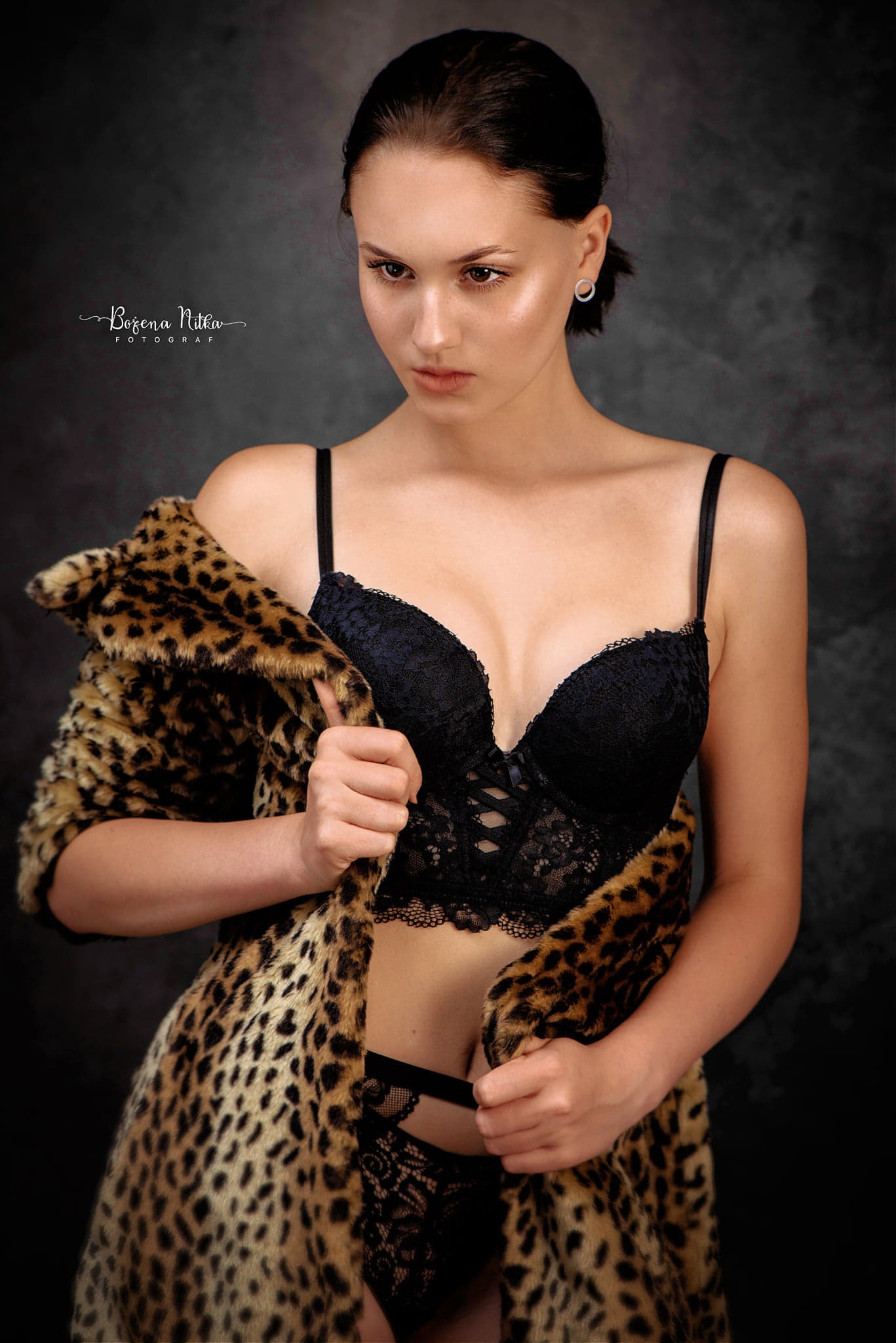 Portret kobiety w czarnej koronkowej bieliźnie i futrze w panterkę na ciemnym tle, delikatny makijaż i minimalistyczna biżuteria.