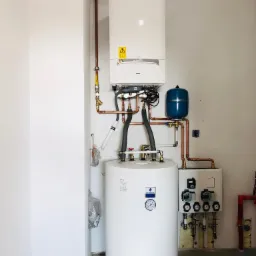 Zestaw kotłowni gazowej z kondensacyjnym kotłem De Dietrich AMC 25kW, emaliowanym zasobnikiem SRK 100L, grupą pompową MT12 na 2 obiegi, widoczne miedziane rury i armatura, całość zamontowana...