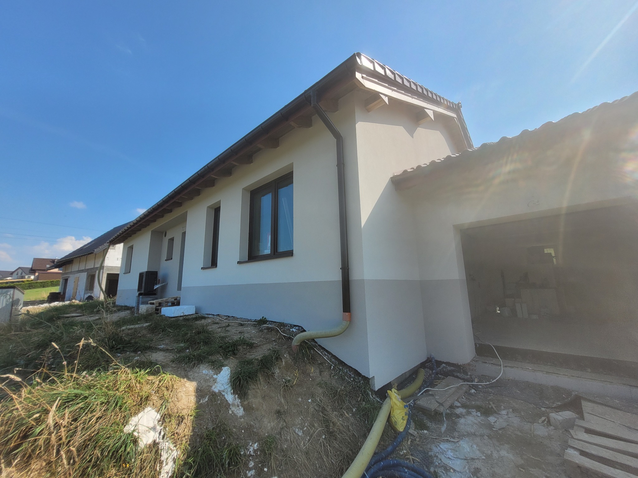 Dom jednorodzinny po remoncie elewacji, z widoczną dwukolorową fasadą i elementami wykończeniowymi. Ujęcie z dołu, na pierwszym planie teren budowy.