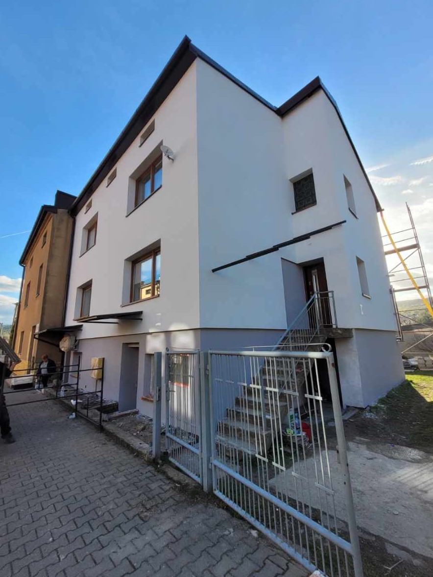 Odnowiona elewacja budynku w Zembrzycach, z widocznymi schodami wejściowymi i fragmentem rusztowania. Jasna kolorystyka i świeże malowanie.