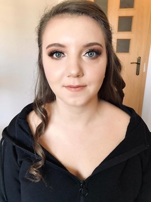 Portret kobiety z profesjonalnym makijażem oczu w odcieniach brązu i beżu, delikatnym konturowaniem i błyszczącymi ustami, włosy częściowo upięte.