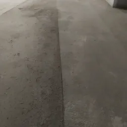 Częściowo wyczyszczona betonowa powierzchnia, kontrastujące obszary brudne i czyste, widoczne ślady wilgoci po myciu.