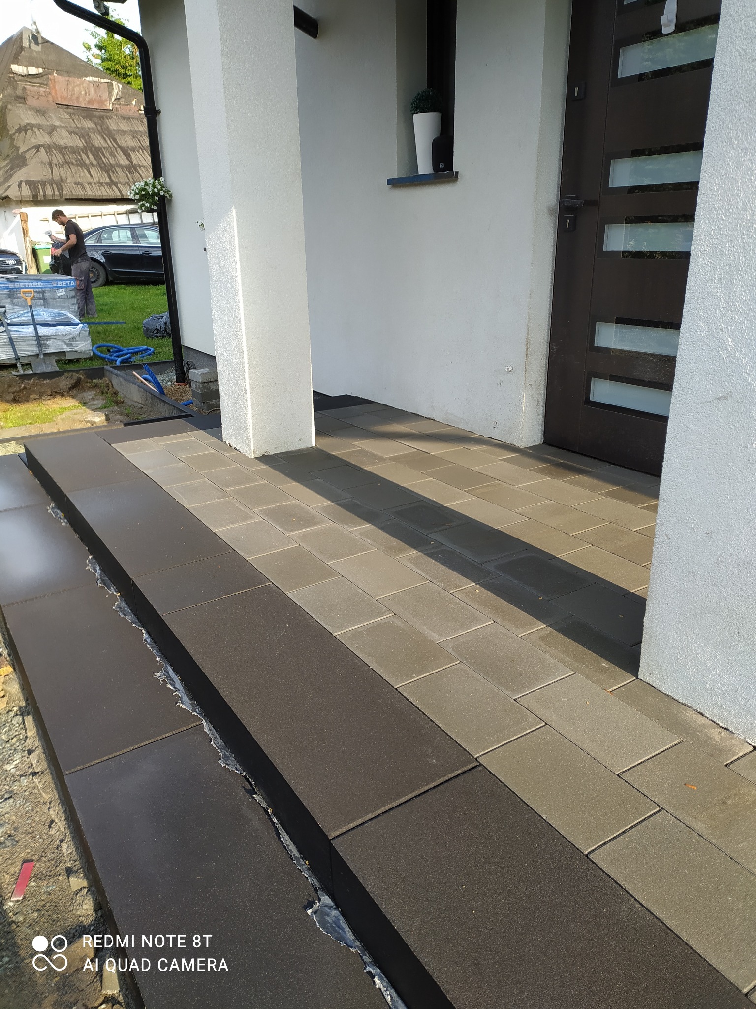 Układanie kostki brukowej w Polanicy-Zdrój: widok na świeżo ułożony fragment schodów wejściowych i chodnika z kostki w dwóch odcieniach szarości, z widocznymi narzędziami i materiałami budowlanymi...