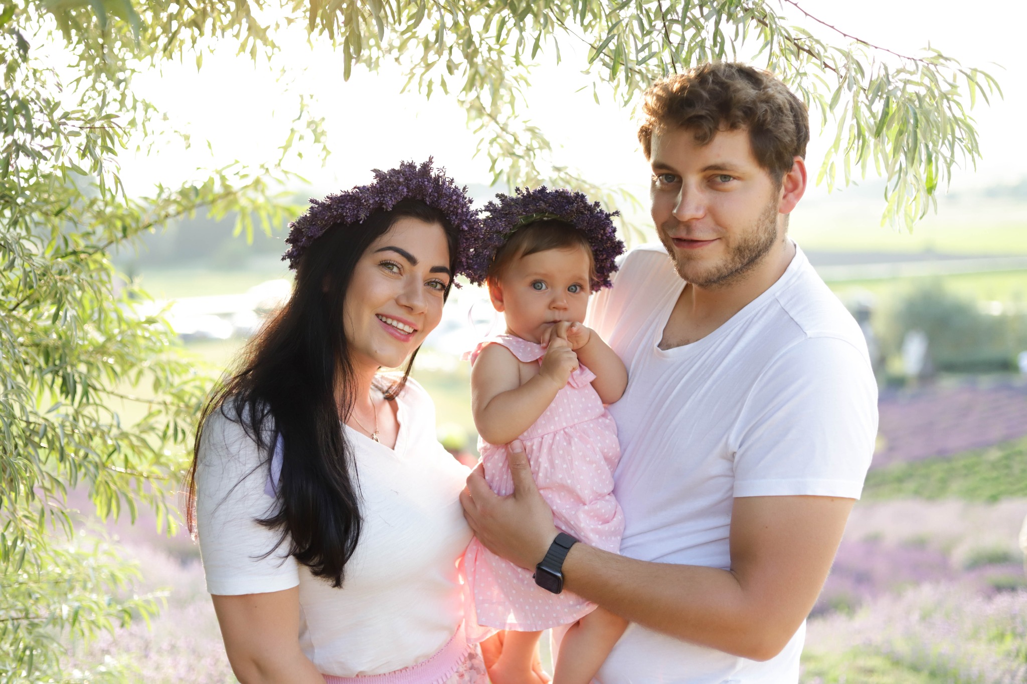 Uśmiechnięta rodzina: mama, tata i córeczka w wiankach z lawendy, na tle kwitnącego pola lawendowego w słoneczny dzień.