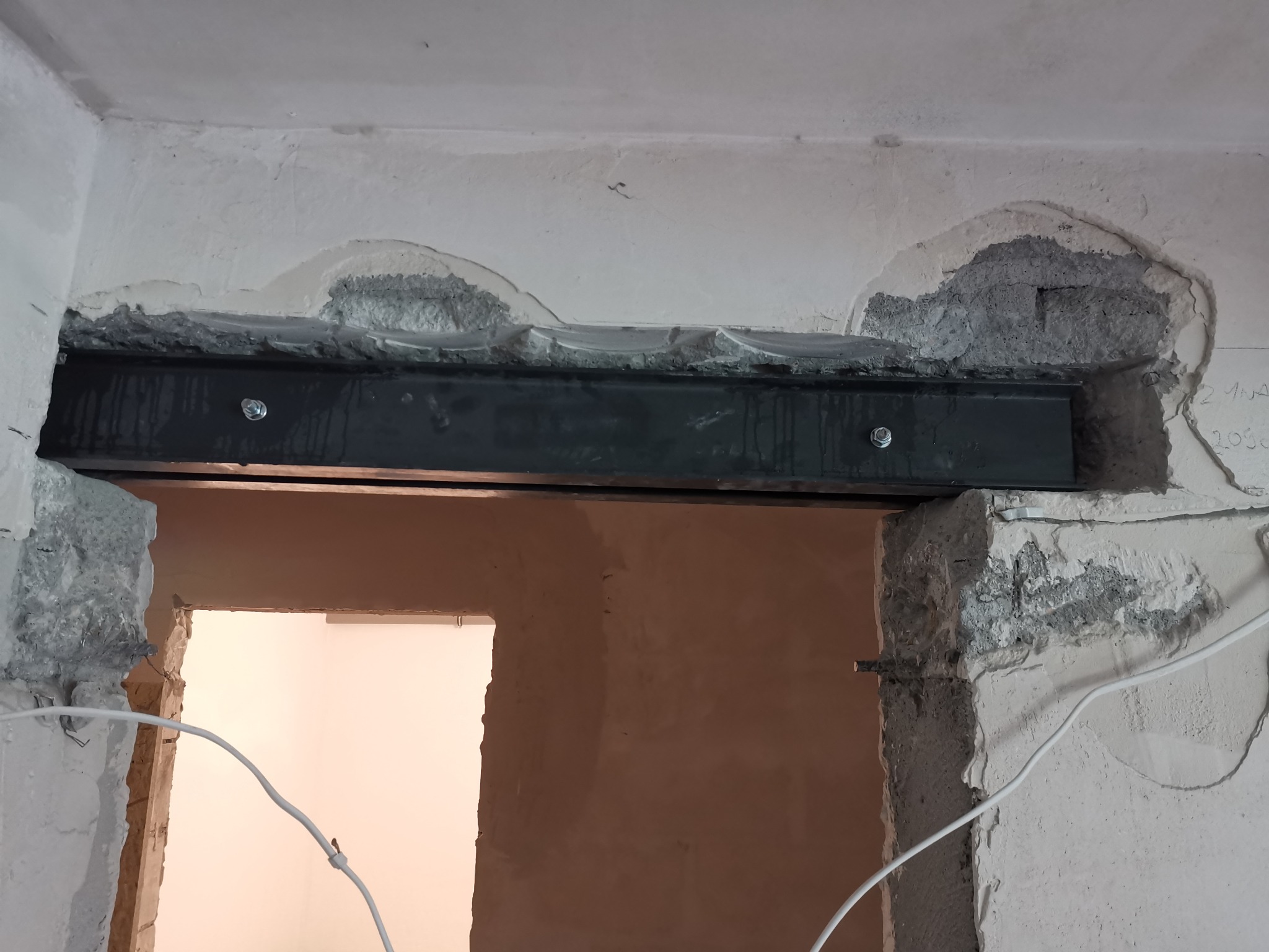 Wzmocnienie otworu drzwiowego stalowym profilem, widoczne ślady po kuciu w surowym tynku, dwa srebrne śruby mocujące.