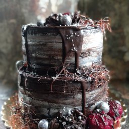 Sweet Kardamoon - Dwupoziomowy tort czekoladowy z abstrakcyjną dekoracją z gałązek, srebrnych kulek i czerwonych owoców, na złotej podkładce.