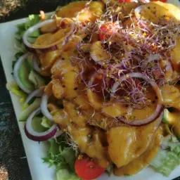 Sałatka z mango w sosie curry, z czerwoną cebulą, pomidorkami koktajlowymi i kiełkami, podana na białym talerzu.