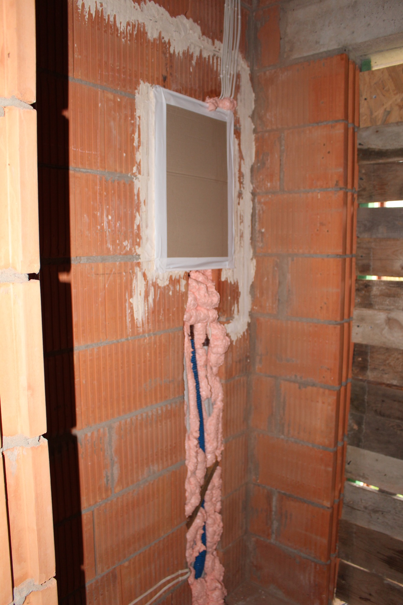 Murowana ściana z cegły dziurawki z otworem okiennym uszczelnionym pianką montażową i instalacją elektryczną zabezpieczoną pianką.