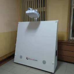 Biała obudowa interaktywnego urządzenia prezentacyjnego z logo 'knooker' i zamontowanym projektorem Epson na wysięgniku, ustawiona w pomieszczeniu z żaluzjami pionowymi.