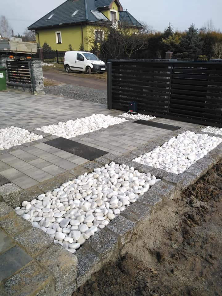 Ułożona kostka brukowa w połączeniu z białymi kamieniami ozdobnymi tworząca wzór na podjeździe przed domem z automatyczną bramą.