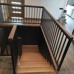 Nowoczesne schody z drewnianymi stopniami i czarną metalową balustradą, widok z góry, parkiet na podłodze, drzwi w tle.