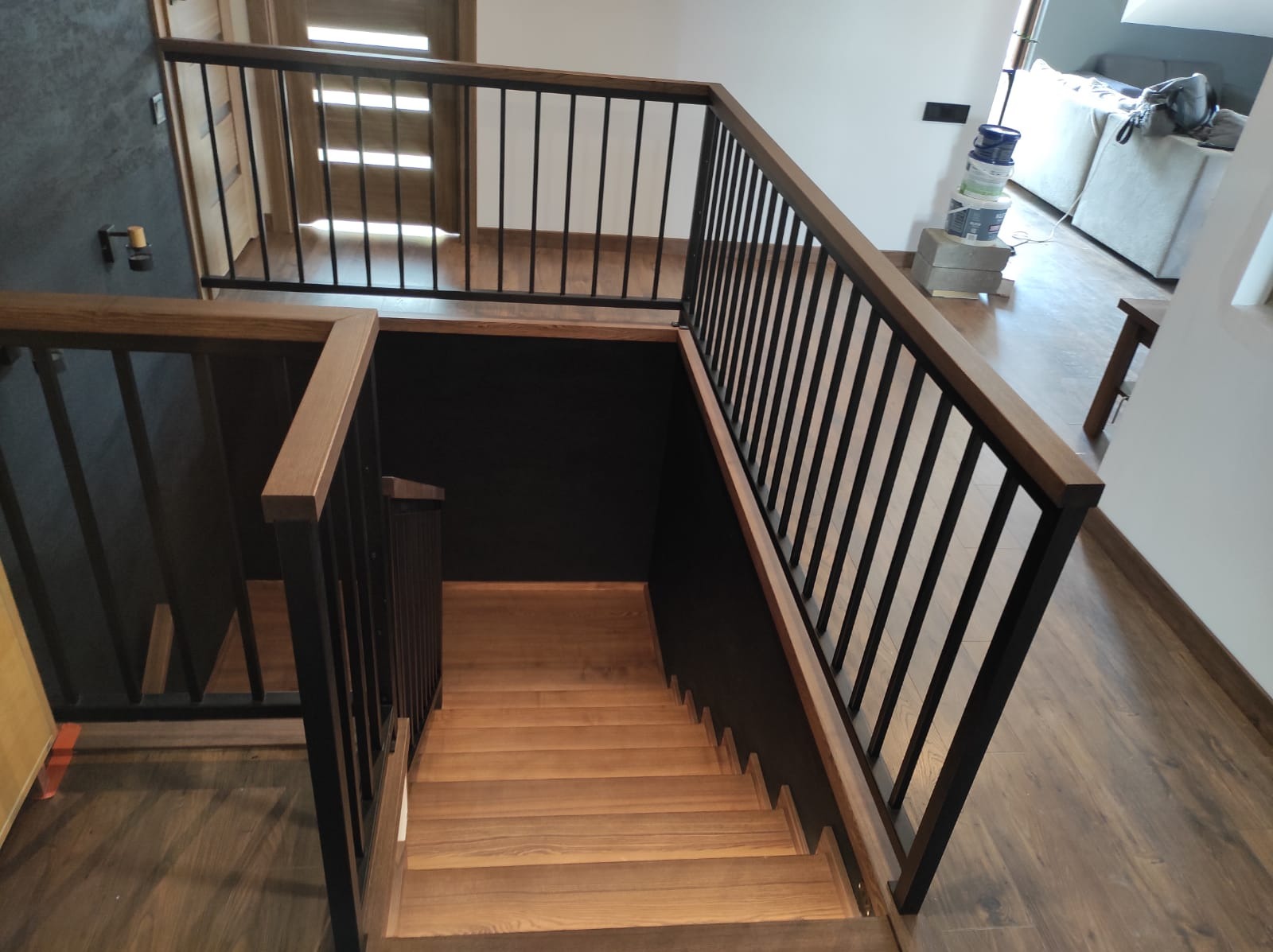 Nowoczesne schody z drewnianymi stopniami i czarną metalową balustradą, widok z góry, parkiet na podłodze, drzwi w tle.