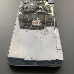 Wymiana Szybki Wrocław - Smartfon Apple iPhone z mocno potłuczoną szklaną obudową, widoczne pęknięcia i ubytki szkła, uszkodzone narożniki i odsłonięte wnętrze obok aparatu.
