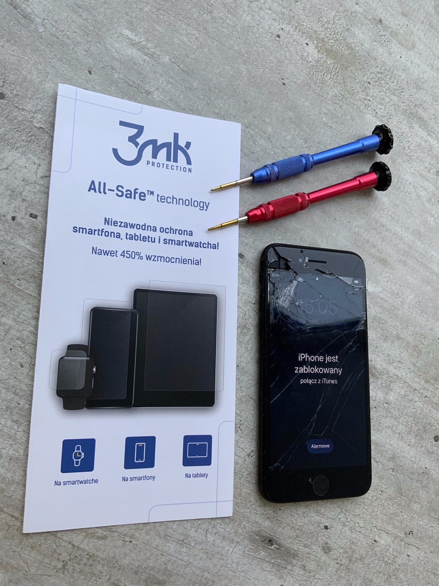 Rozbity iPhone z komunikatem o blokadzie ekranu, leżący obok ulotki reklamującej ochronę ekranu 3mk i dwóch precyzyjnych śrubokrętów z kolorowymi rączkami.
